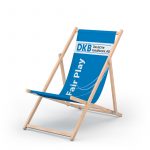 Liegestuhl aus Holz mit blauer Liegefläche und Aufdruck am oberen Rand der liegefläche auf weiß in blau "DKB" und Schwarz "Deutsche Kreditbank AG", Aufdruck links in Weiß von unten nach oben "Fair Play"